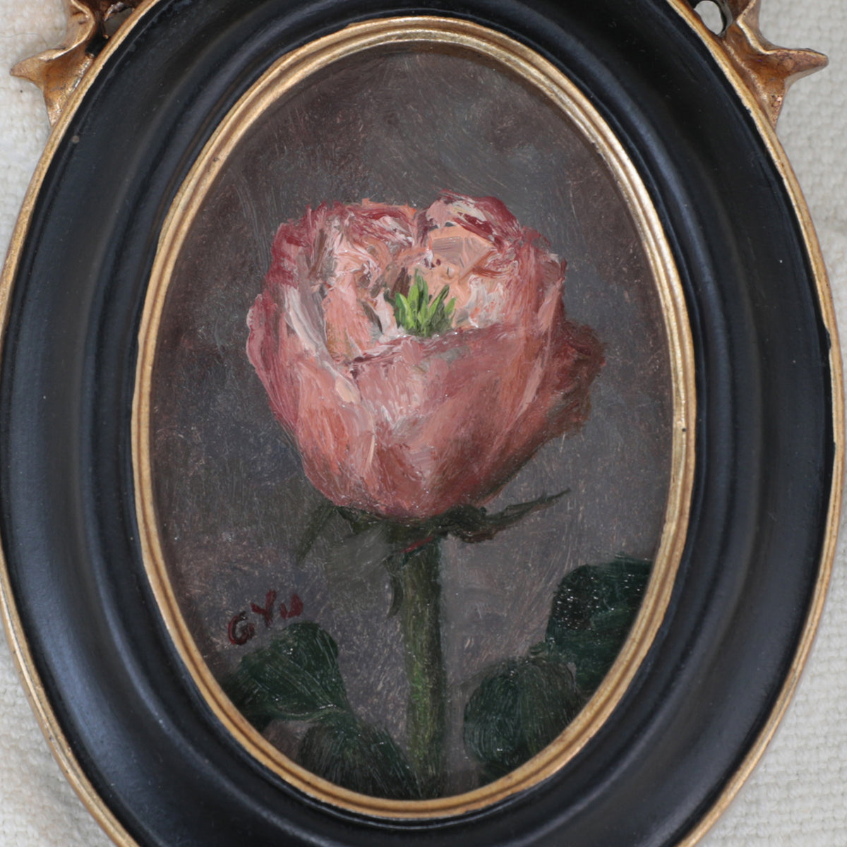 Close up of a miniature pink rose oil painting in a black oval frame with a gilt ribbon bow crest