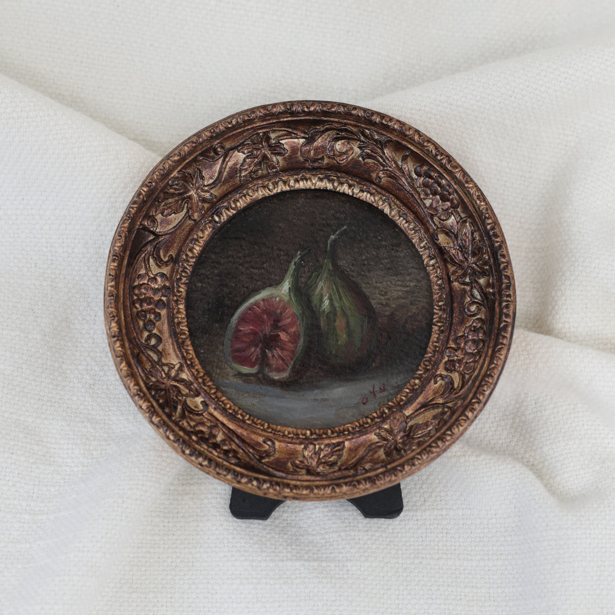 Fig still life oil painting in round gilt frame on cream fabric