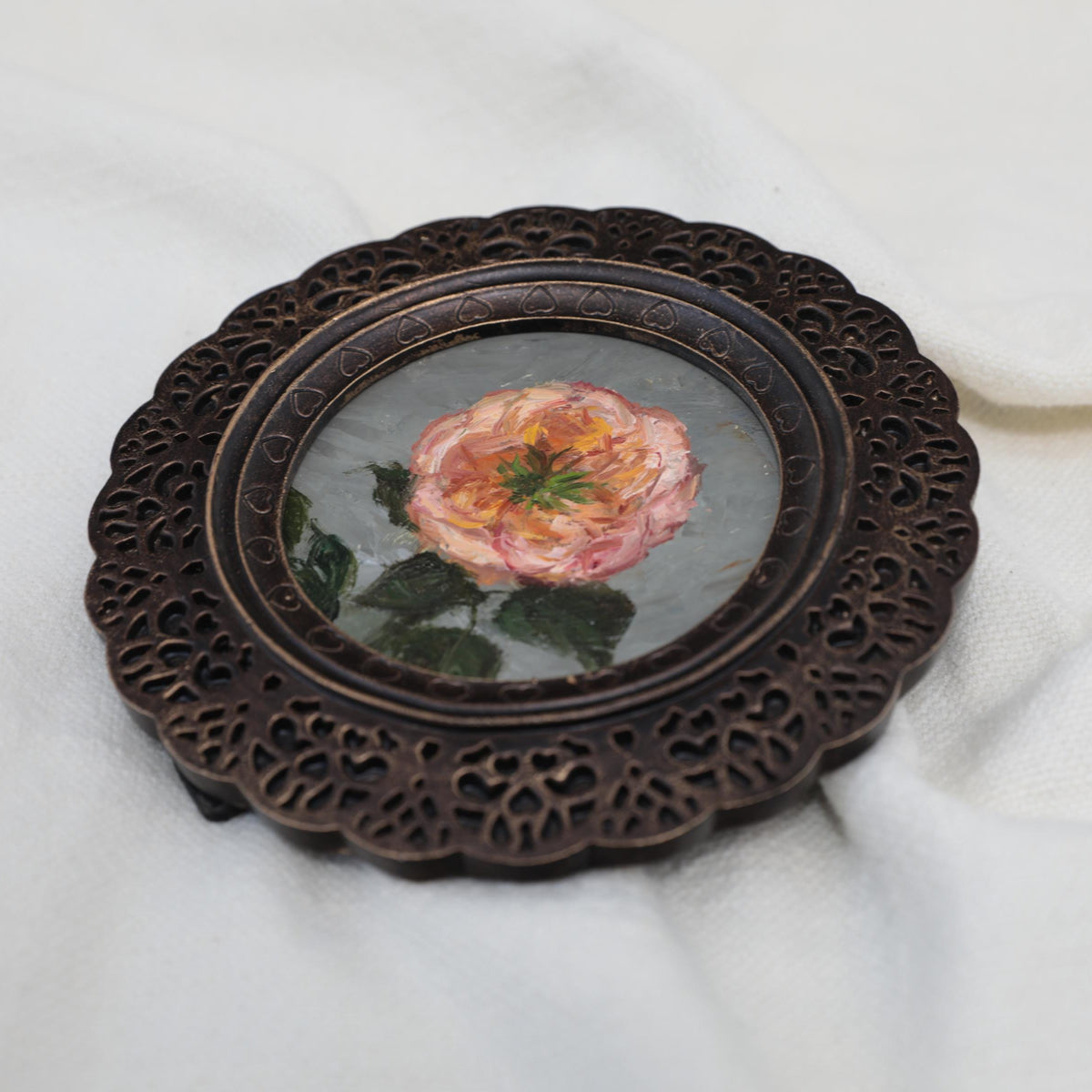 Overhead view of pink rose miniature painting in round openwork frame
