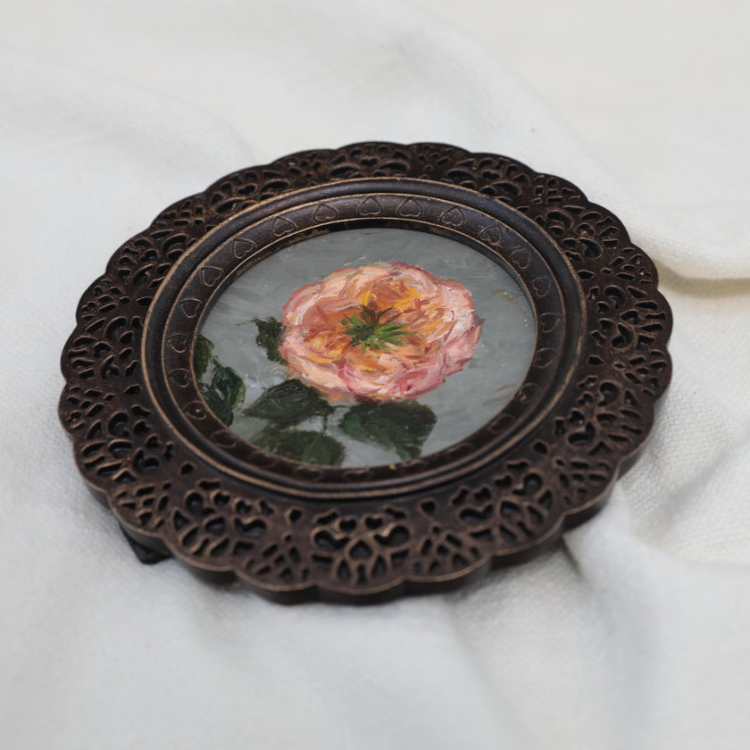 Overhead view of pink rose miniature painting in round openwork frame
