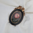 Framed pink rose miniature oil painting resting on cream fabric, showing the gilt bow frame and green leaves