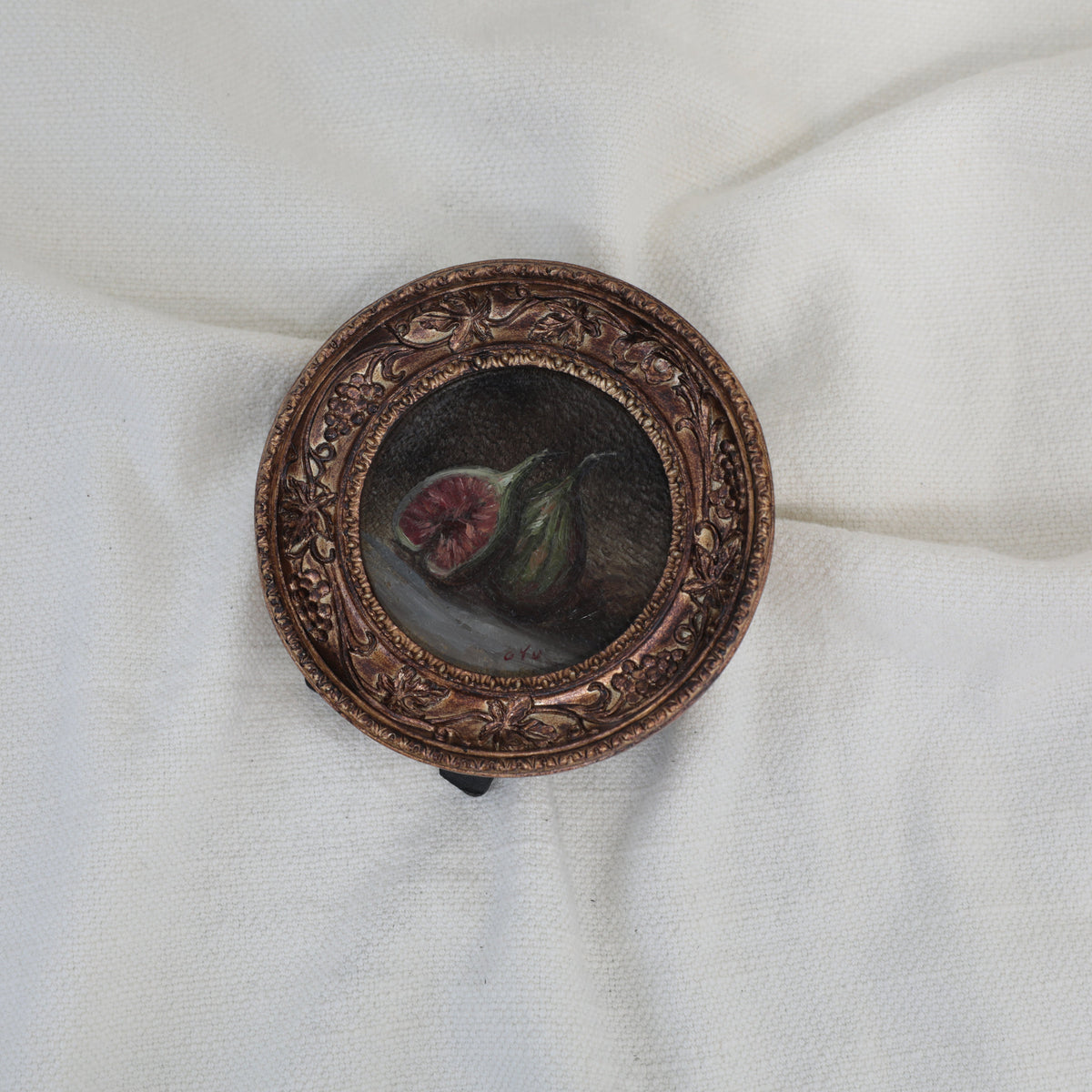 Overhead view of fig still life painting in round gilt frame, zoomed out, second angle