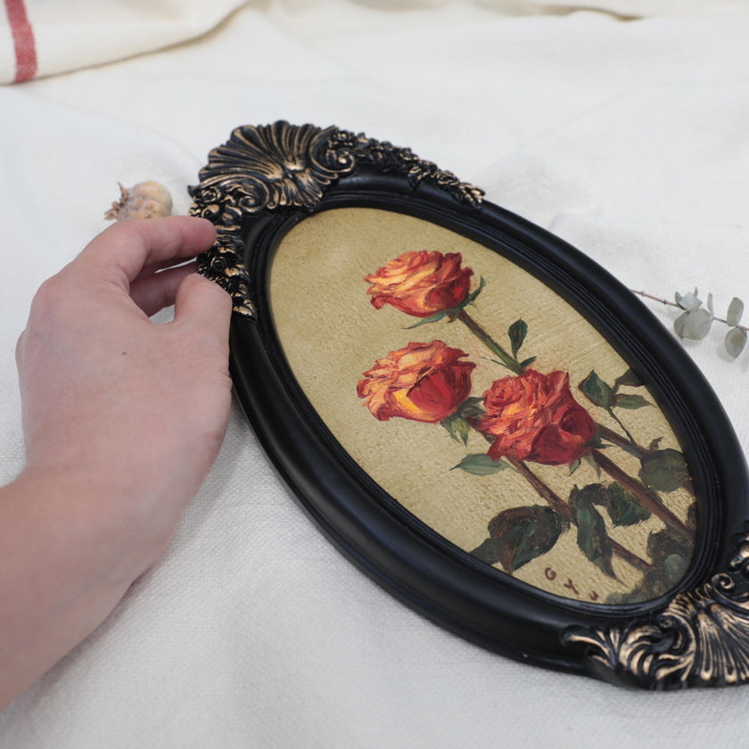 Hand for scale, for original red roses oil painting in an ornate long oval gilt frame on cream linen