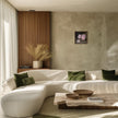 Mockup of the painting in a modern curved white sectional sofa in a sunlit contemporary living room, styled with olive green throw pillows, a marble coffee table, and a textured beige wall.