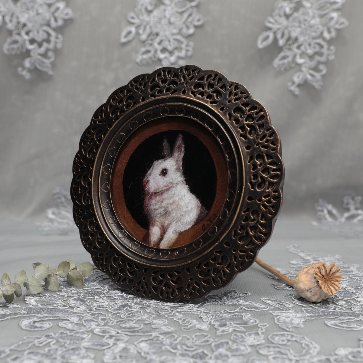 Small framed bunny painting print displayed among dried flowers and lace