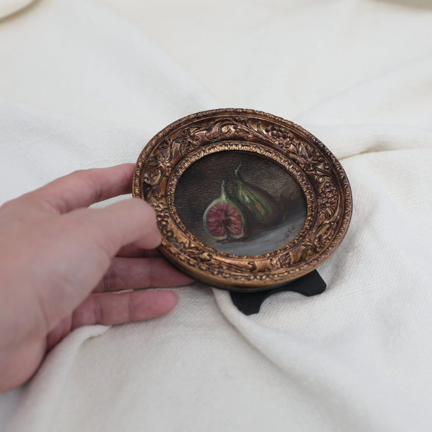 Hand holding round gilt frame with fig still life oil painting for scale comparison 