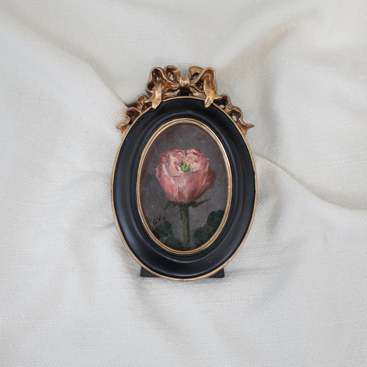Miniature pink rose oil painting in an oval black and gilt frame with a ribbon bow, another view