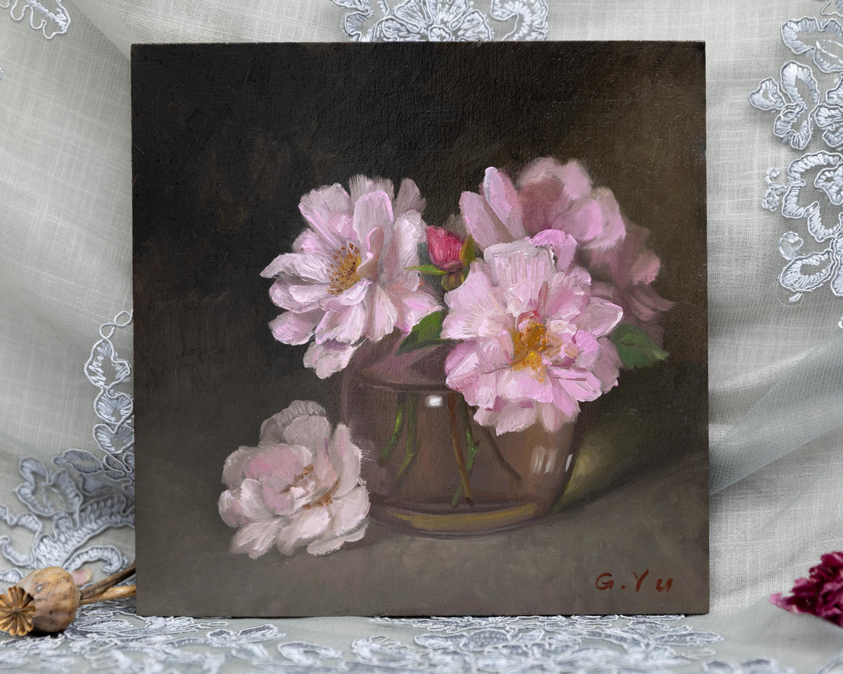 A square oil painting of pale pink flowers in a brown vase against a dark brown background, displayed on a white lace-draped surface with dried botanical props.