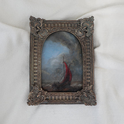 Original seascape painting of a red sailing boat on choppy water beneath a dark cloudy sky in an ornate bronze vintage-style frame