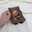 Original pink rose oil painting in an long narrow gilt frame on cream linen, side view with hand for scale. 