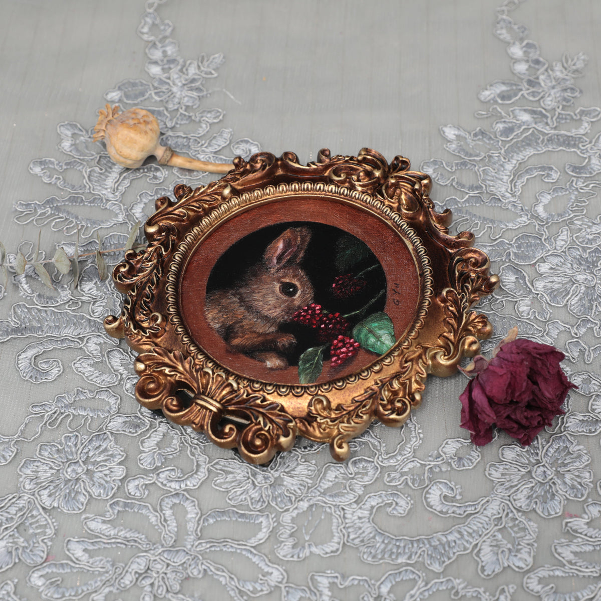 Framed bunny painting print laid flat with dried rose and poppy pod