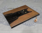 Side view of the canvas painting of a black cat with yellow eyes on a warm brown background, displayed on a white lace cloth with a small dried flower prop.