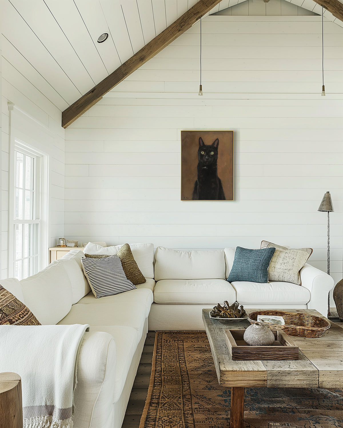 Framed custom black cat oil portrait hanging above a white sectional sofa in a vaulted-ceiling living room
