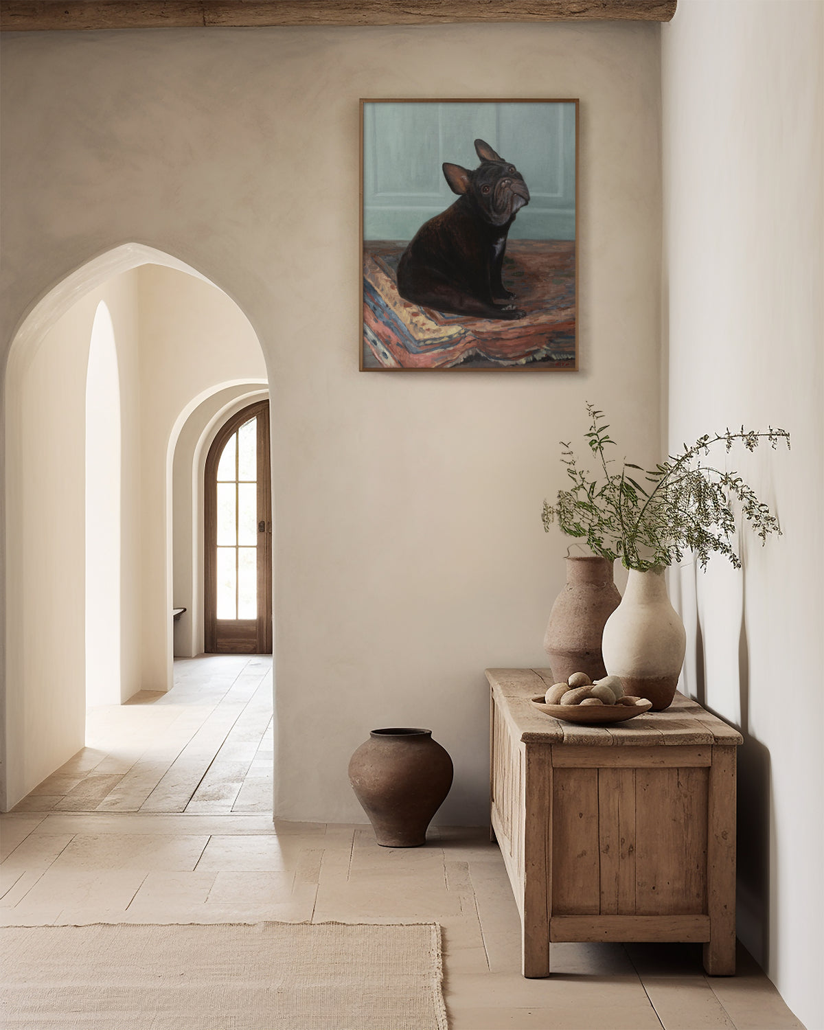 Framed French bulldog oil portrait hanging in a plaster hallway near arched doorways and stoneware vases