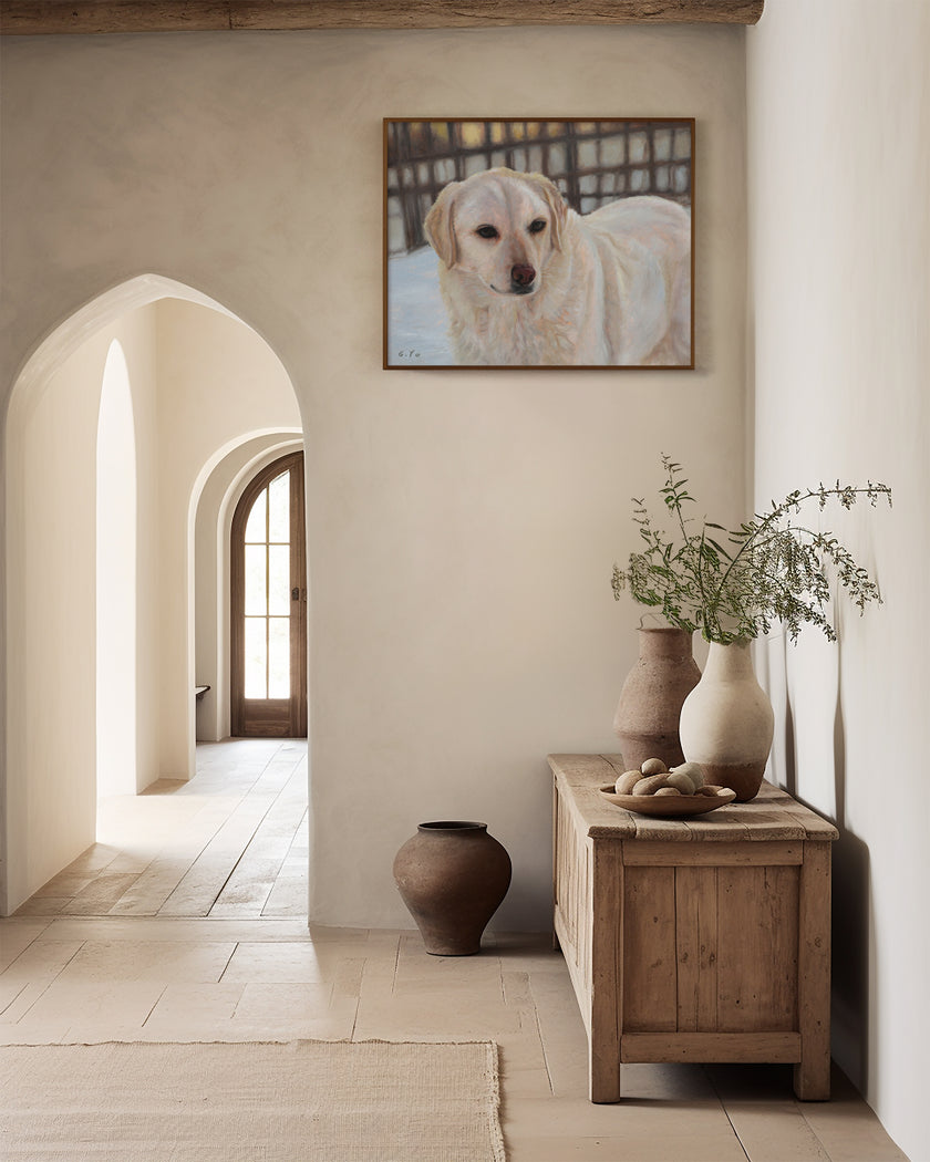 Oil painting of a cream-colored retriever hangs on a warm beige plaster wall in a rustic, sunlit room with arched doorways, a wooden console table, and ceramic vases.
