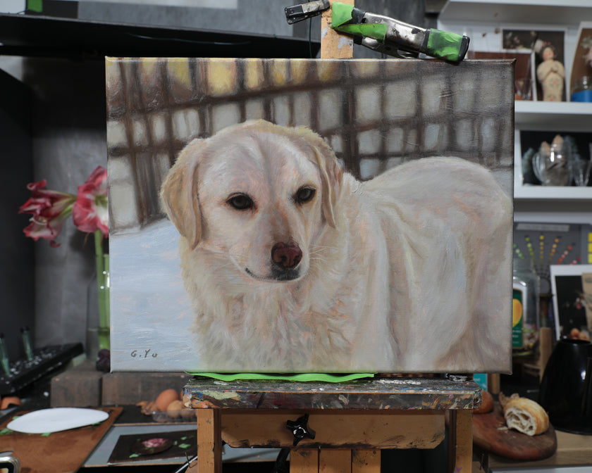 A canvas painting of a golden retriever dog, displayed on an easel in an artist's studio with art supplies and shelves in the background.