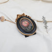 Side view of the original pink rose oil painting in an ornate oval gilt frame on cream linen with a dried poppy pod and eucalyptus