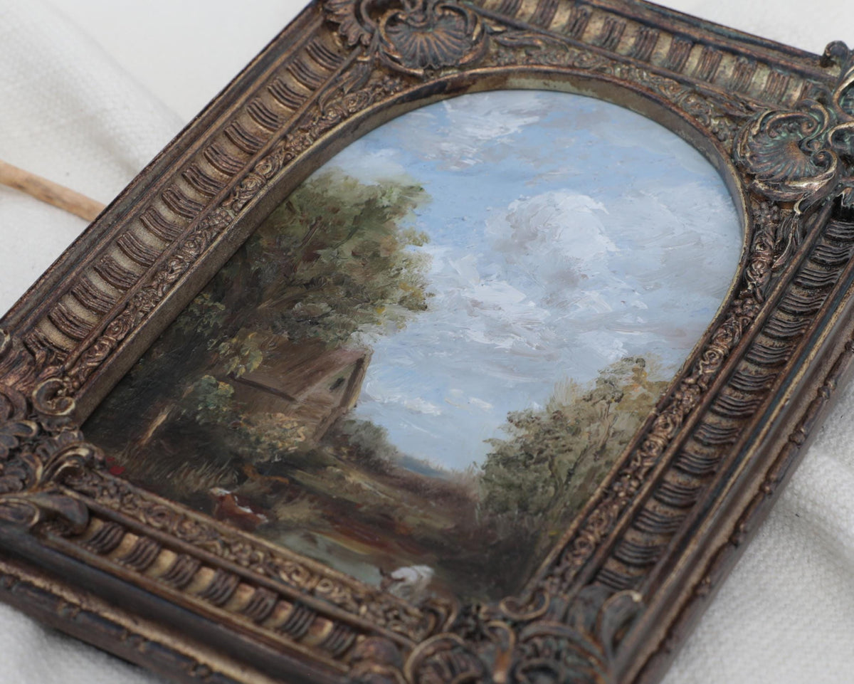 Side view of an original miniature antique-style framed landscape painting with an ornate dark brown carved frame, displayed on a draped white fabric background.