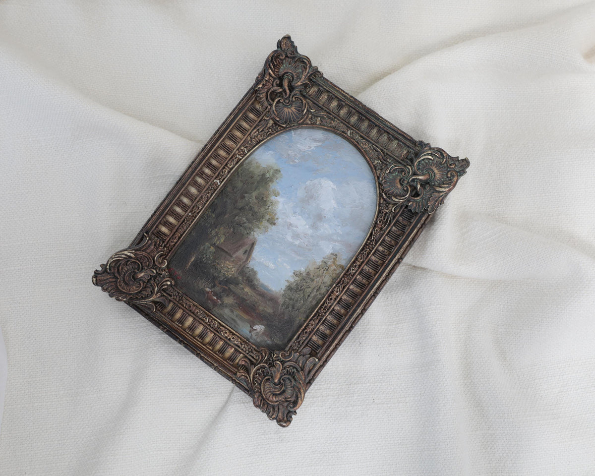 Miniature antique-style framed landscape painting with an ornate dark brown carved frame, displayed on a draped white fabric background.