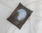 Miniature antique-style framed landscape painting with an ornate dark brown carved frame, displayed on a draped white fabric background.