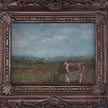 Close up of the miniature framed landscape painting of a cow grazing in a field, set in an ornate dark bronze frame