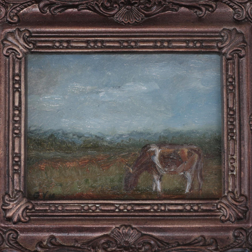 Close up of the miniature framed landscape painting of a cow grazing in a field, set in an ornate dark bronze frame