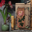 Pink rose miniature oil painting on an oval panel, taped to an easel in the artist's studio