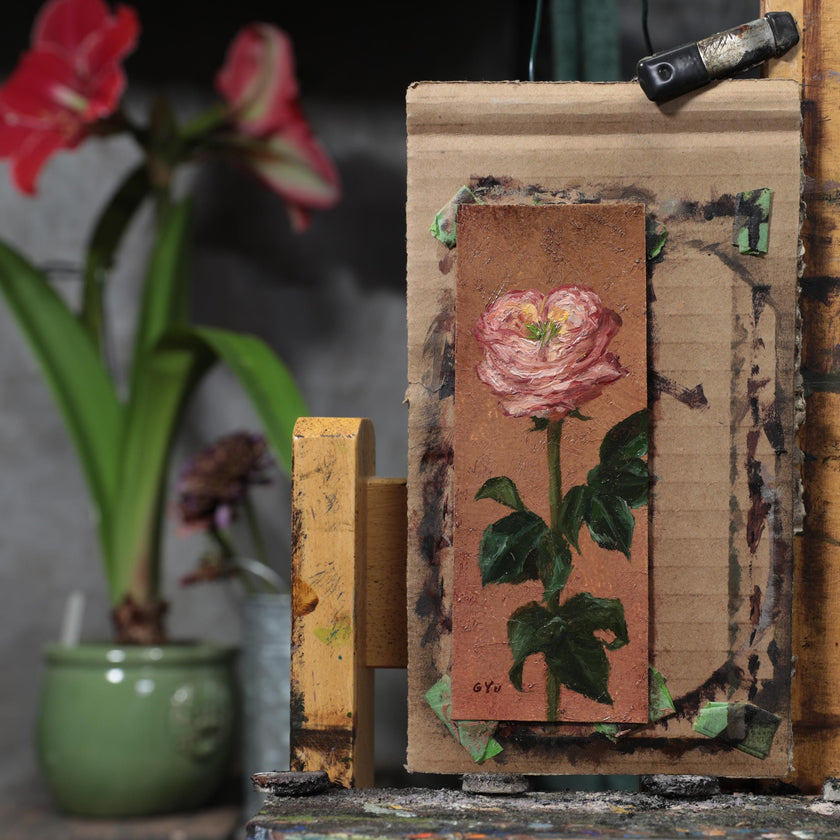 Pink rose miniature oil painting on an oval panel, taped to an easel in the artist's studio