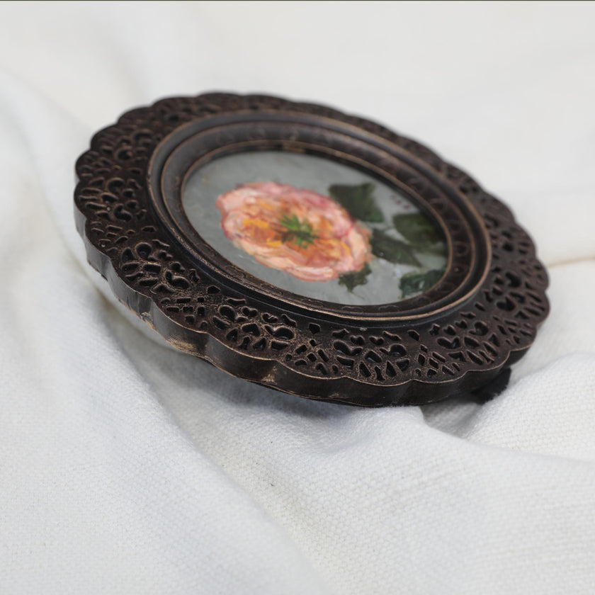 Angled view of round framed pink rose painting on cream linen