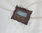Different angle of the miniature framed landscape painting of a cow grazing in a field, set in an ornate dark bronze frame