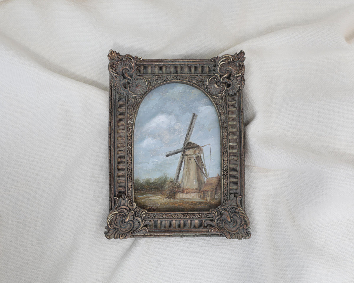 zoomed out original countryside landscape painting of a rustic windmill under a cloudy blue sky in an ornate bronze vintage-style frame