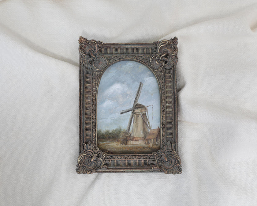 zoomed out original countryside landscape painting of a rustic windmill under a cloudy blue sky in an ornate bronze vintage-style frame