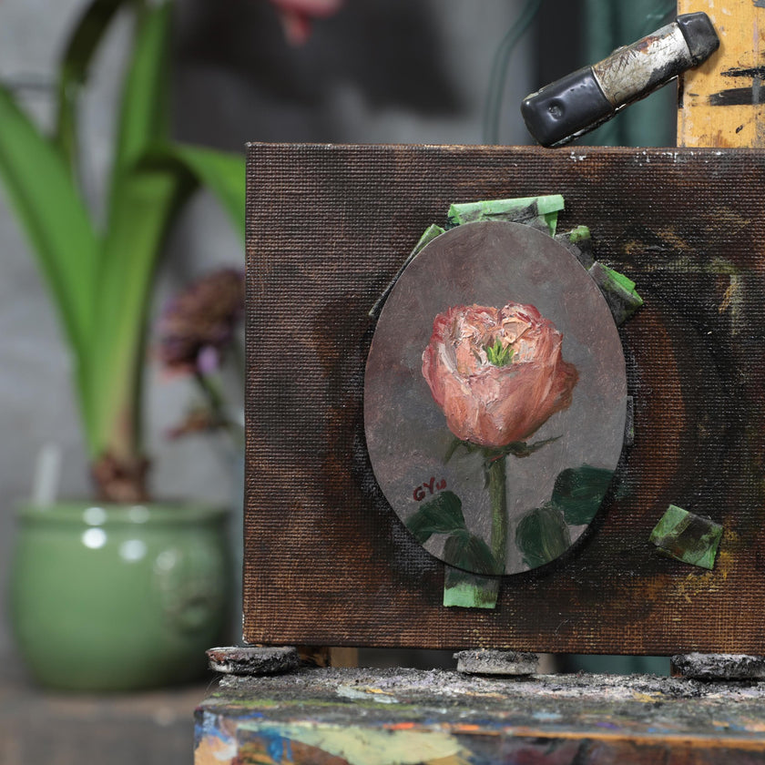 Pink rose miniature oil painting on an oval panel, taped to an easel in the artist's studio