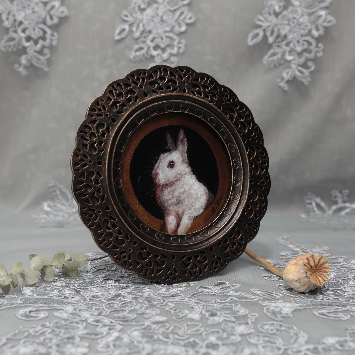 Small framed bunny painting print displayed among dried flowers and lace