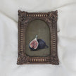Small still life oil painting of two purple figs, one halved, on an olive-green background in an arched ornate vintage-style frame