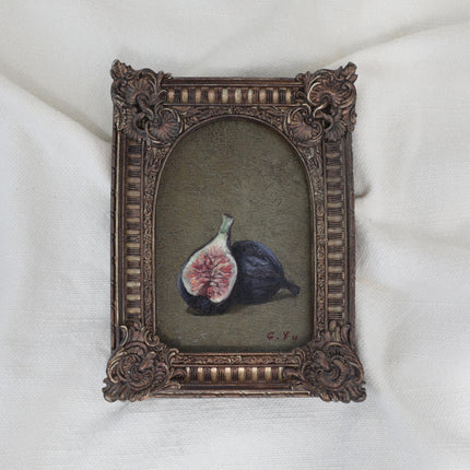 Small still life oil painting of two purple figs, one halved, on an olive-green background in an arched ornate vintage-style frame