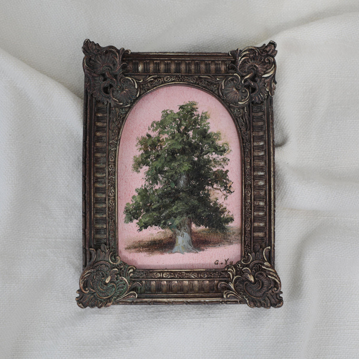 Small oil painting of a green tree on a pink background in an arched ornate vintage-style frame