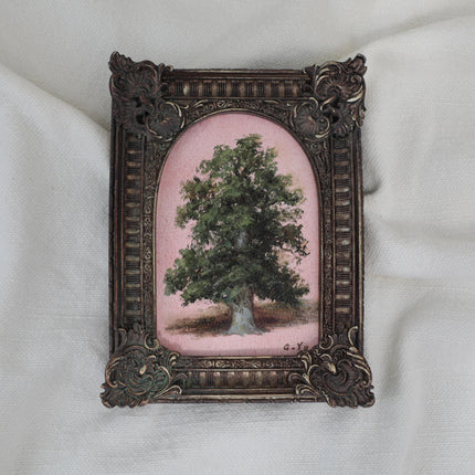 Small oil painting of a green tree on a pink background in an arched ornate vintage-style frame