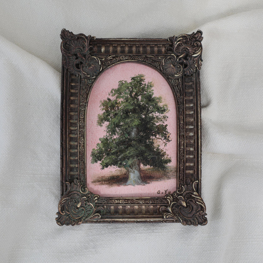 Small oil painting of a green tree on a pink background in an arched ornate vintage-style frame