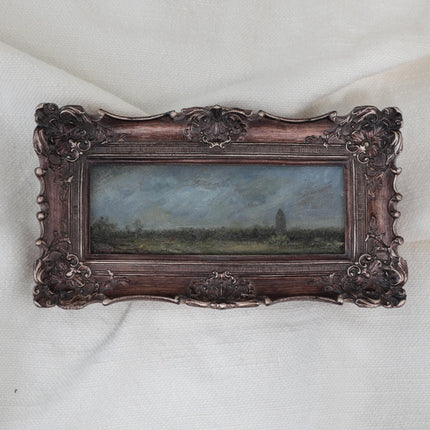 Small moody landscape oil painting of a stormy sky over green fields and a distant tower in an ornate vintage-style frame