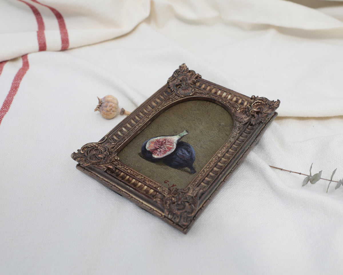 Angled view of an Old Master inspired fig still life painting in an ornate frame beside dried flowers