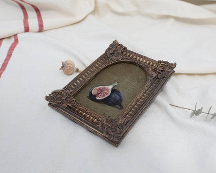 Angled view of an Old Master inspired fig still life painting in an ornate frame beside dried flowers