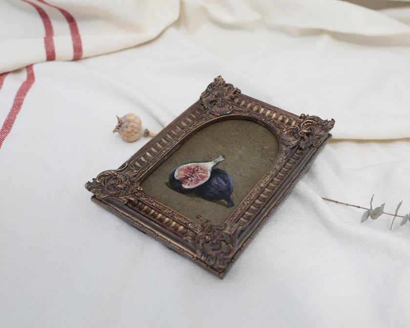 Angled view of an Old Master inspired fig still life painting in an ornate frame beside dried flowers