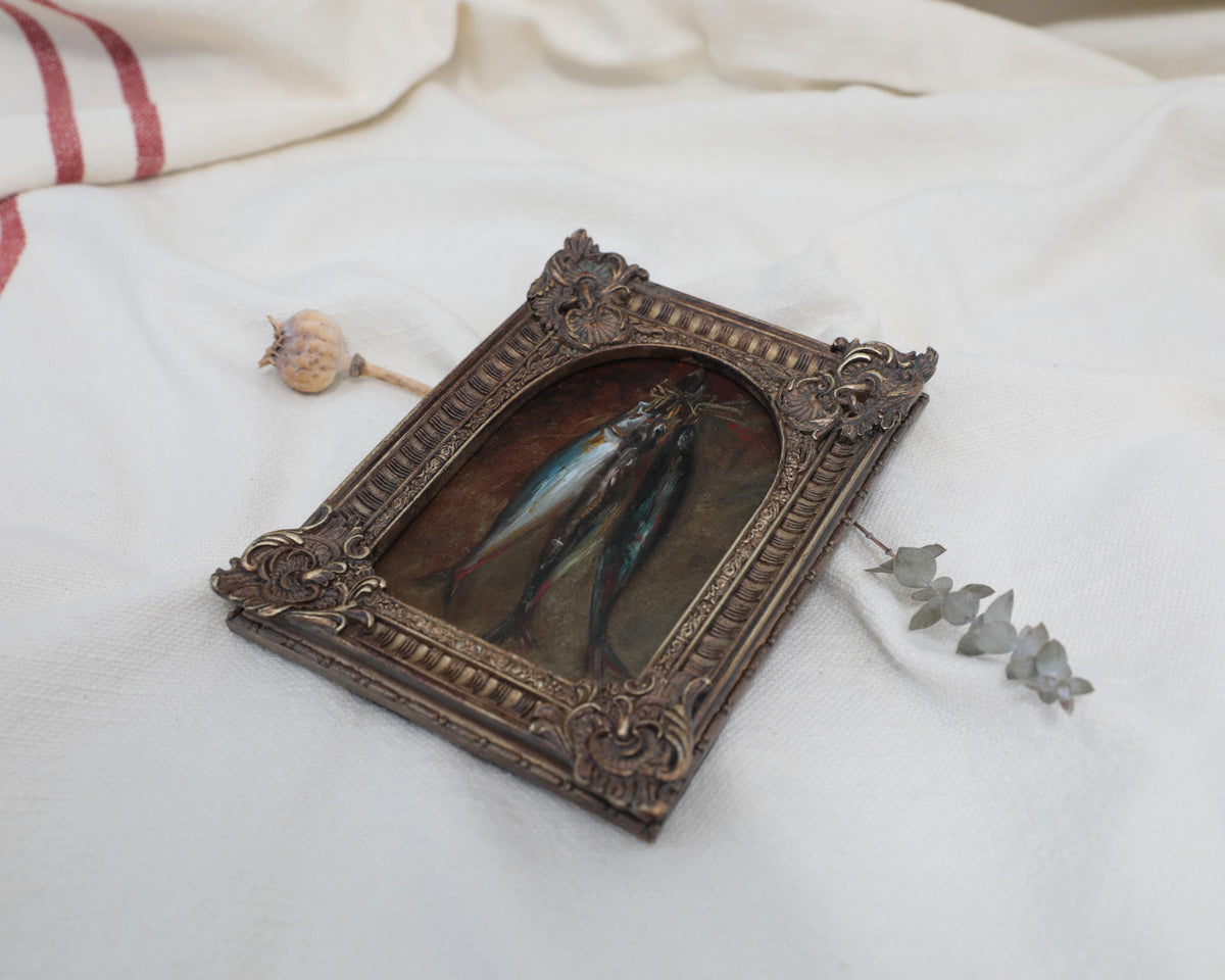 Angled view of an Old Master inspired fish still life painting in an ornate frame beside dried flowers