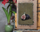Unframed fig still life oil painting on an easel in the artist's studio beside a potted plant