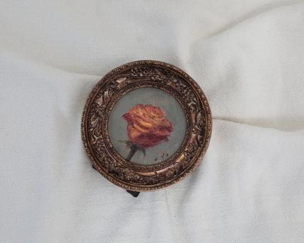 Original rose oil painting in a round vintage-style frame displayed on a small black stand