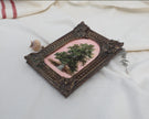 Angled view of a vintage-style tree oil painting in an ornate frame beside dried flowers
